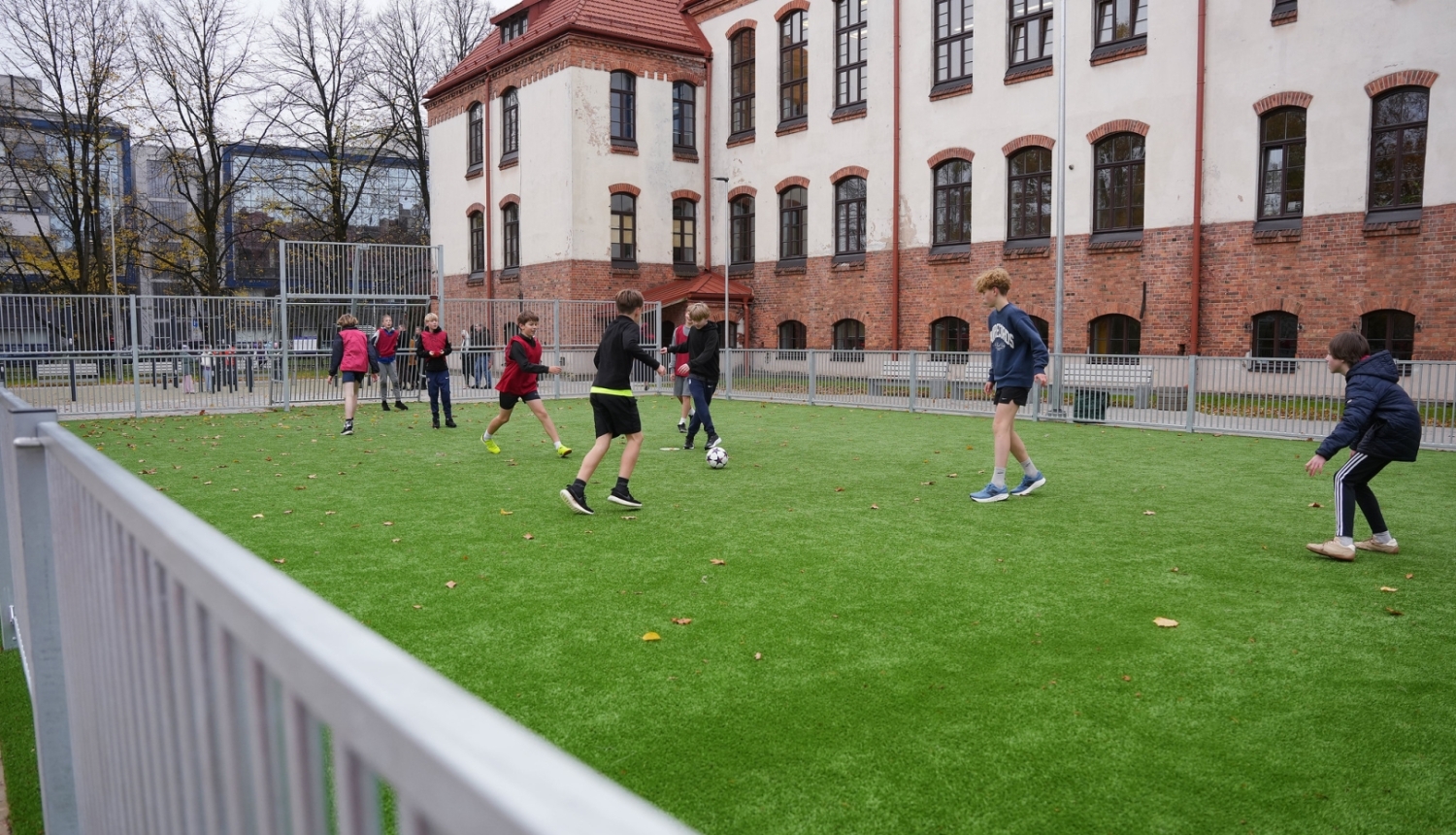 Bērni spēlē futbolu sporta laukumā