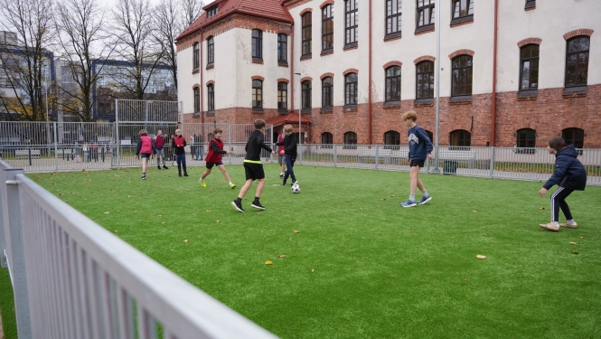 Bērni spēlē futbolu sporta laukumā