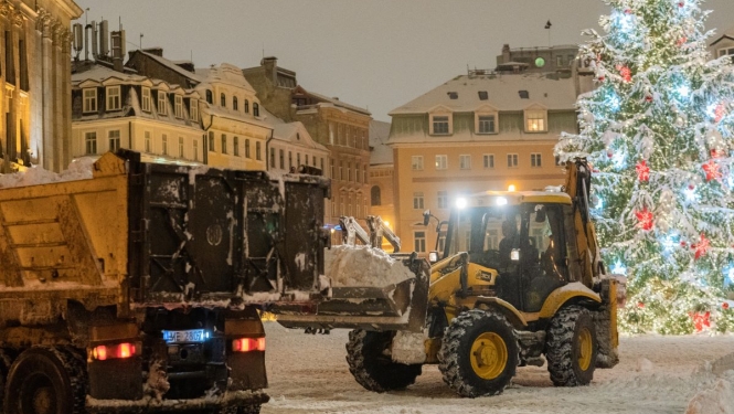 Traktors kravas mašīnā krauj sniegu