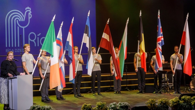 Cilvēki uz skatuves ar dažādu valstu karogiem rokās