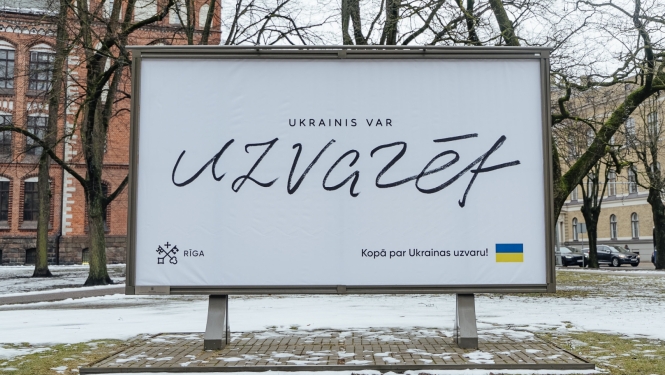 Ukrainas atbalsta plakāts pilsētvidē ar uzralstu "Ukrainis var uzvarēt"