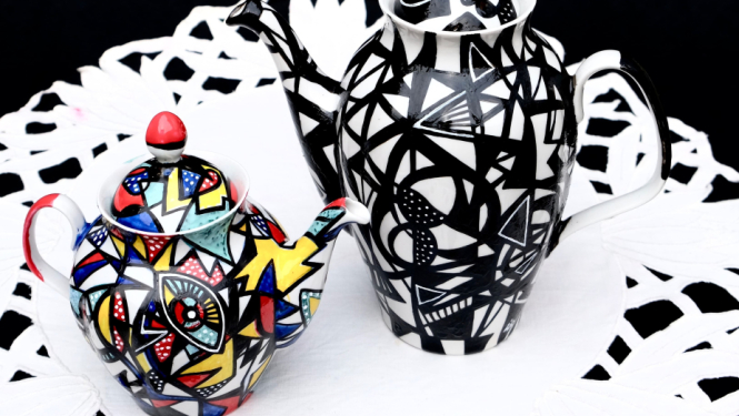 Ievas Blūmas apgleznotas porcelāna kannas, novietotas uz mākslinieces vecvecmammas izšūtā galdauta. 