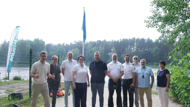 Cilvēki fotografējas pie Bābelīša ezra zilā karoga