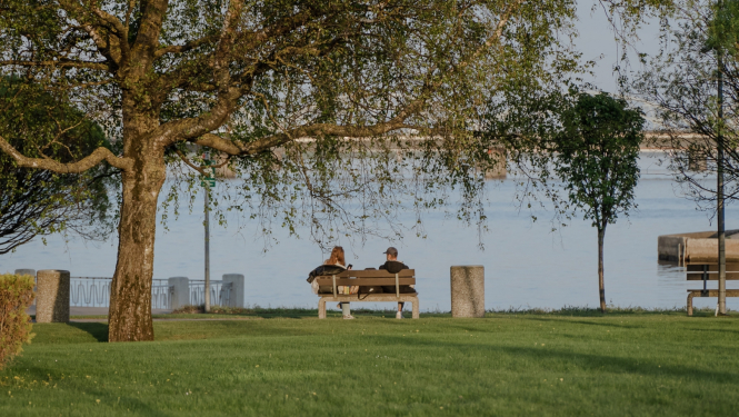 Cilvēki sēž uz soliņa krastmalā