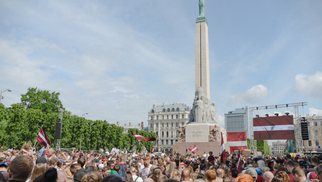 Daudz cilvēku ar karogiem rokjās pie Brīvības pieminekļa