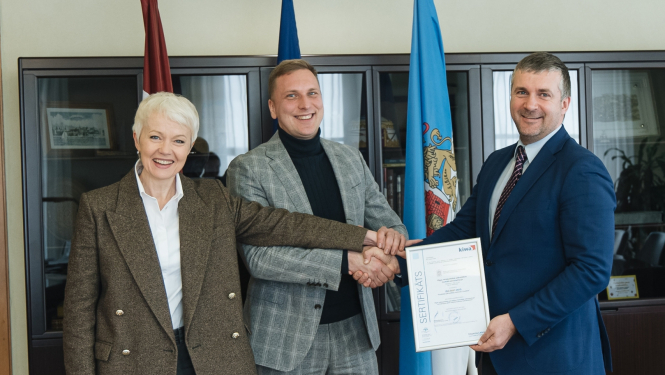 Cilvēki tur rokās rāmīti ieliktu ISO sertifikātu