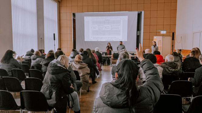Cilvēki sēž zālē un skatās prezentāciju