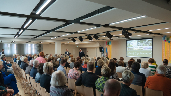 Cilvēki sēž zālē un skatās prezentāciju