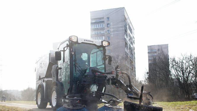 Traktors ar birstēm vāc smiltis no trotuāra