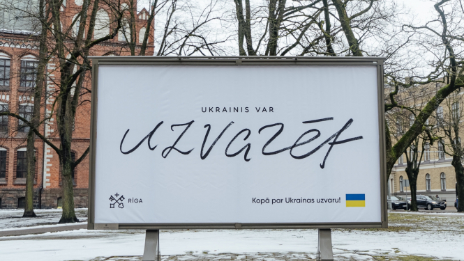 Ukrainas atbalsta plakāts pilsētvidē ar uzralstu "Ukrainis var uzvarēt"