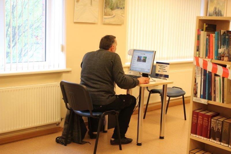 Cilvēks sēž pie datora bibliotēkā