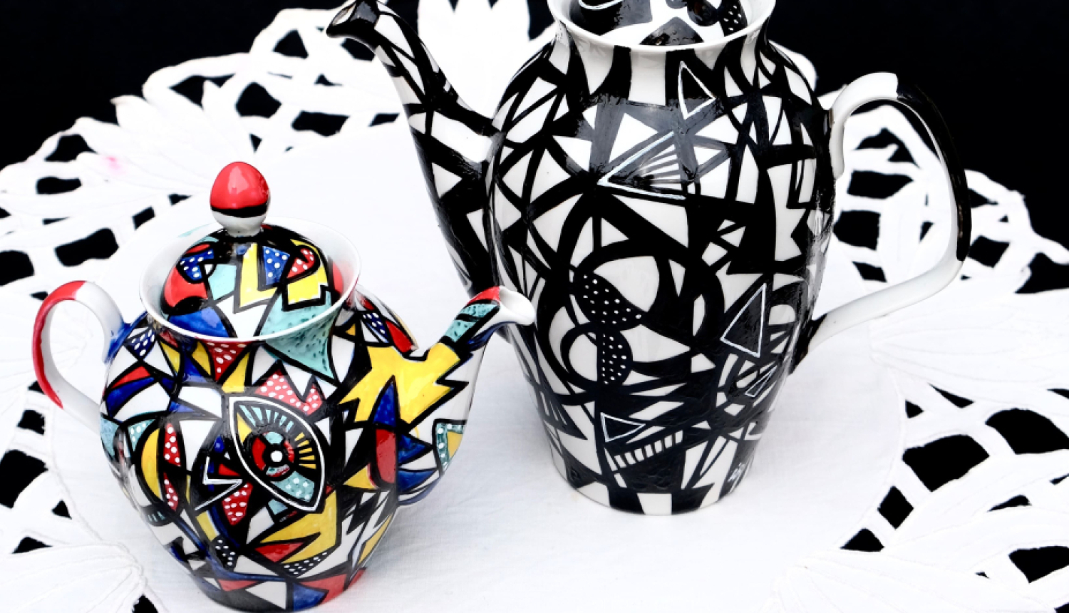 Ievas Blūmas apgleznotas porcelāna kannas, novietotas uz mākslinieces vecvecmammas izšūtā galdauta. 