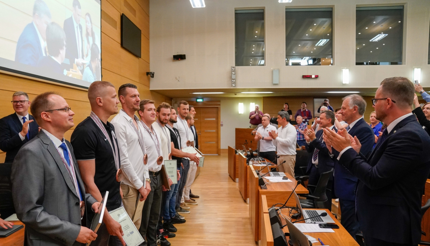 Cilvēki stāvot kājās sveic sportistus