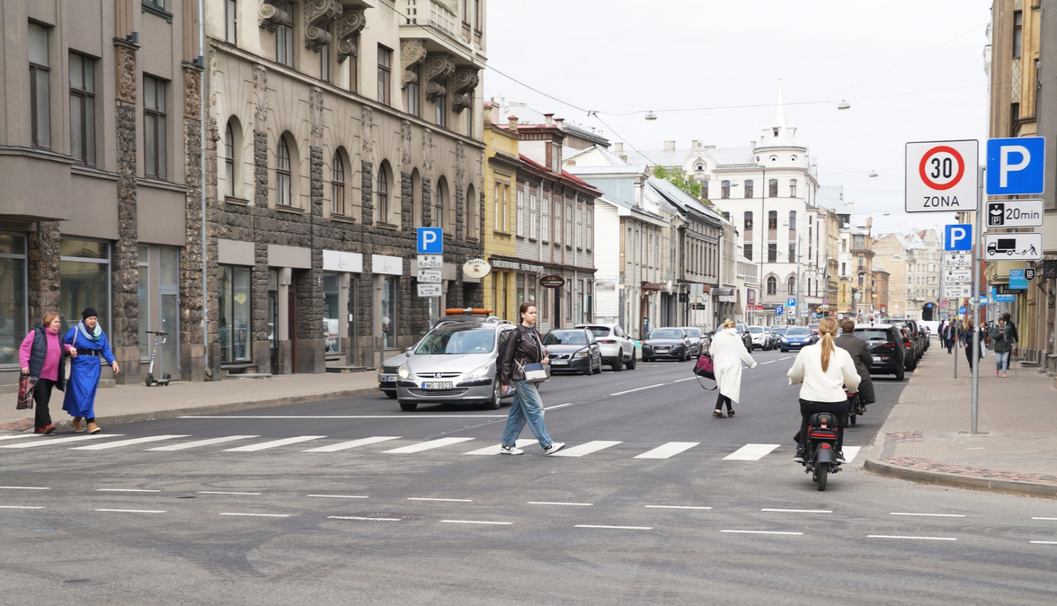 Auto brauc un cilvēki iet pa Matīsa ielu