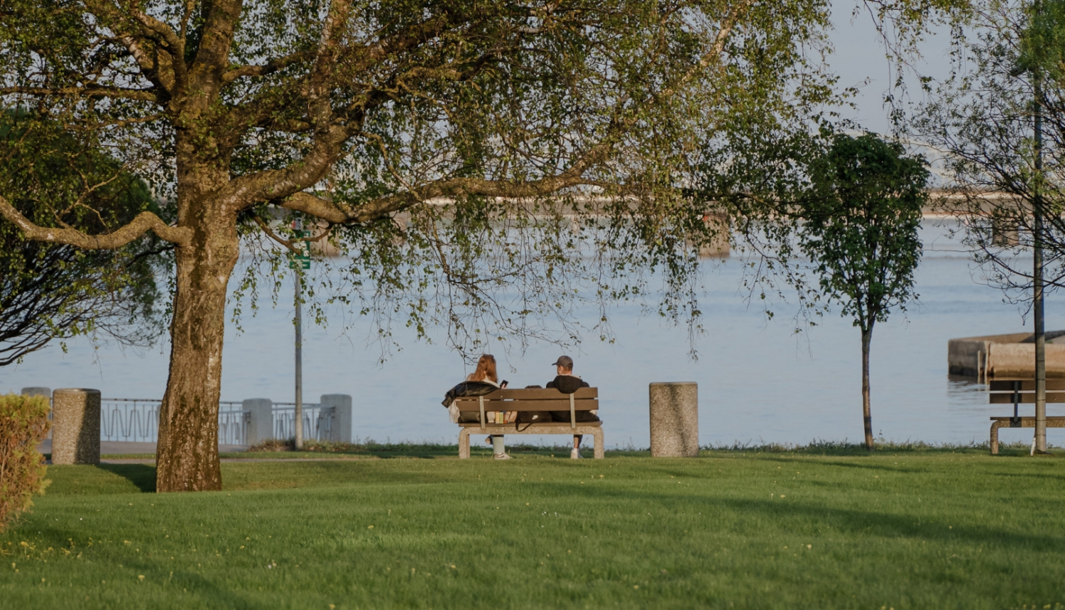 Cilvēki sēž uz soliņa krastmalā