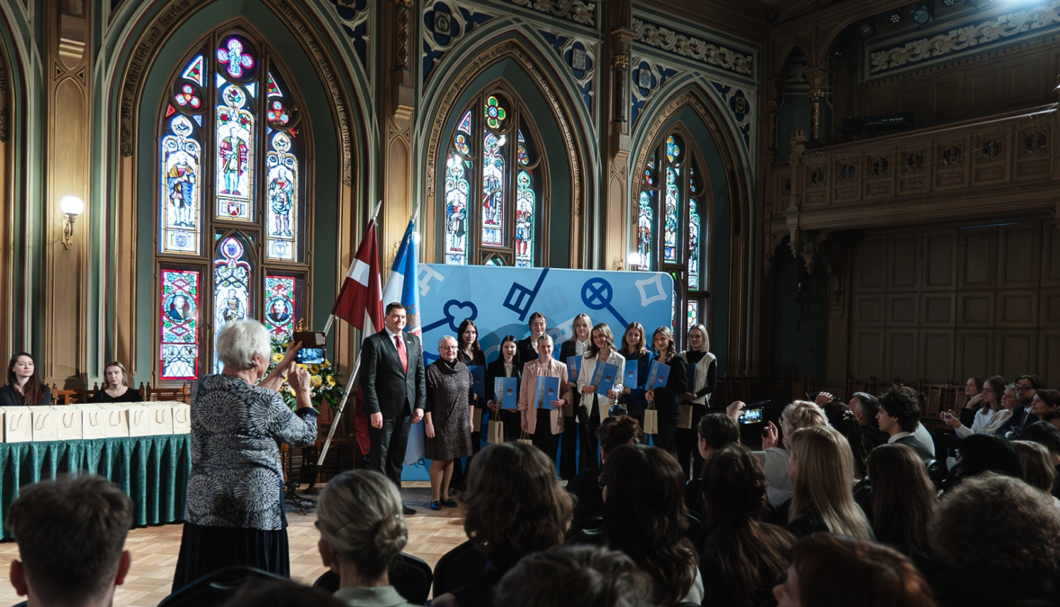 Apbalvotie skolēni fotografējas skatuves priekšā