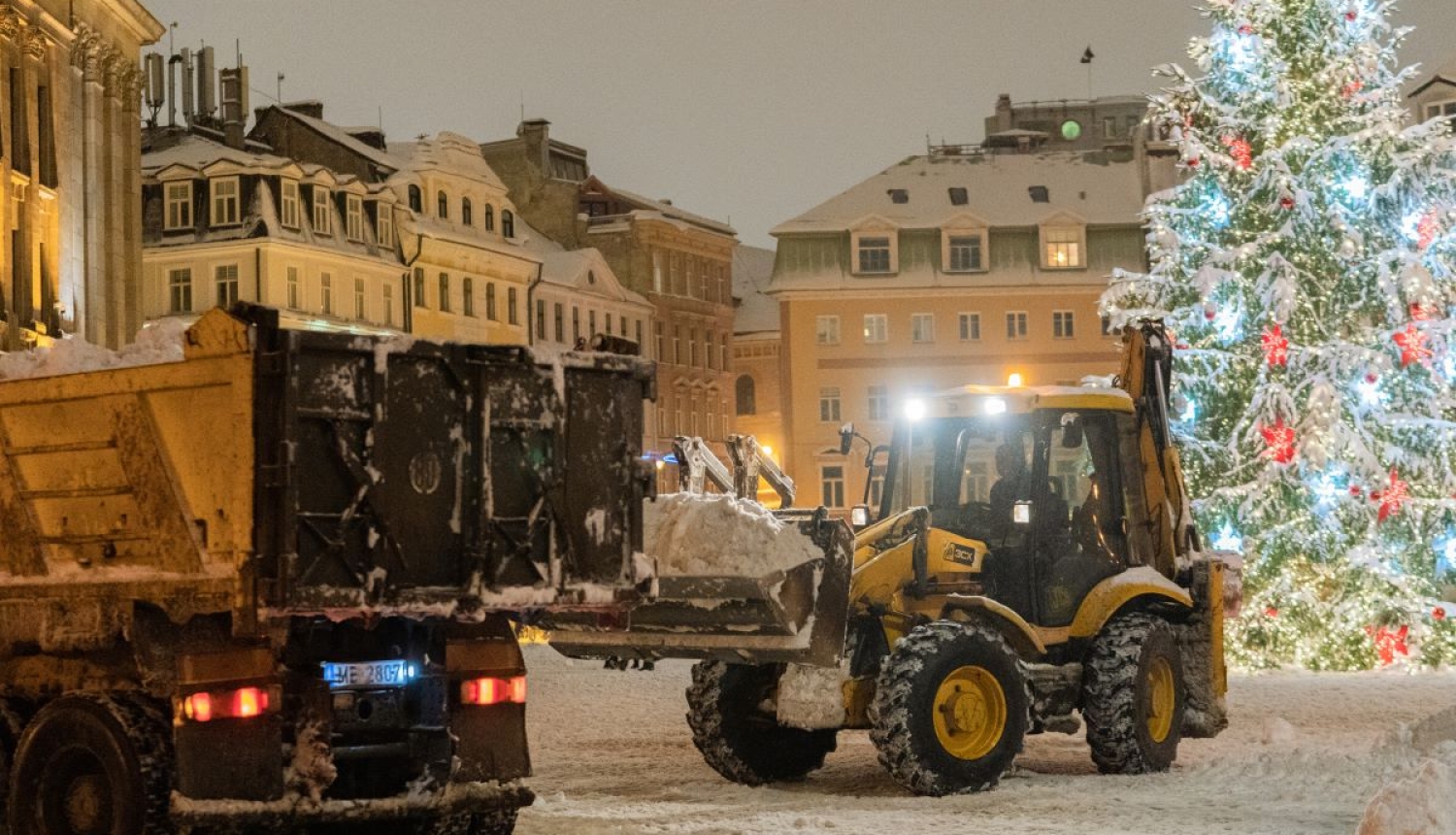 Traktors kravas mašīnā krauj sniegu