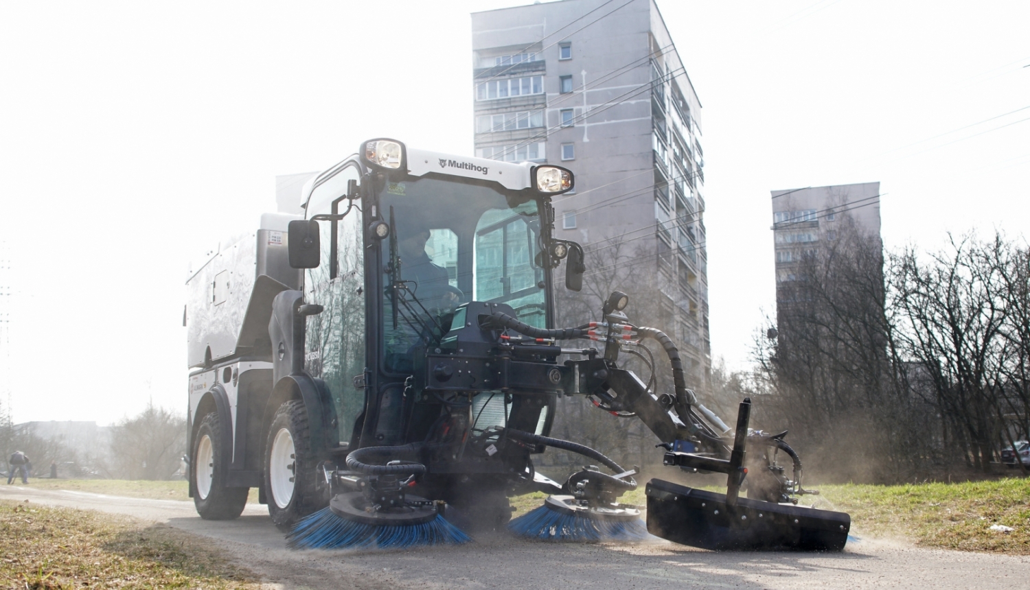 Traktors ar birstēm vāc smiltis no trotuāra